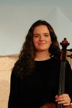 Woman with brown hair, black shirt, and cello looking at camera