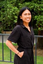 Woman with long dark hair, in dark clothing, standing outside.