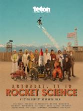 Professional skiers and riders from Teton Gravity Research (TGR) pose in various costumes in a group shot with a skier doing a backflip above them while holding flaming torches. The title of the ski film is Actually, It Is Rocket Science.
