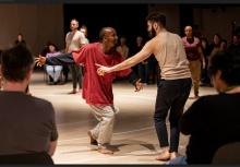 Two people dancing, facing each other, in front of an audience