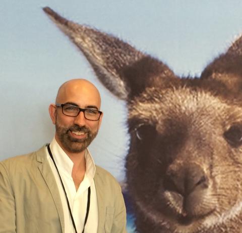 Man wearing glasses standing next to a picture of a kangaroo
