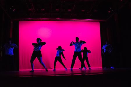Sillouette of 4 people dancing against a bright pink background