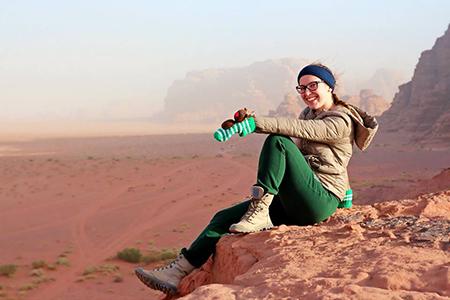 Photograph of a person sitting on a cliff in a desert landscape
