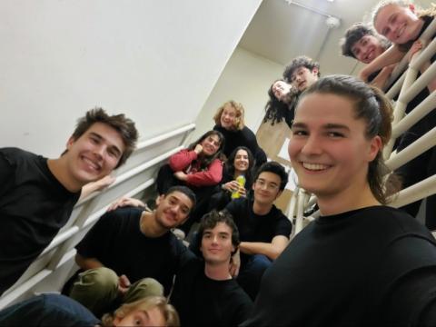 Photo of the comedy members in a stairwell, standing, sitting and leaning over the railing