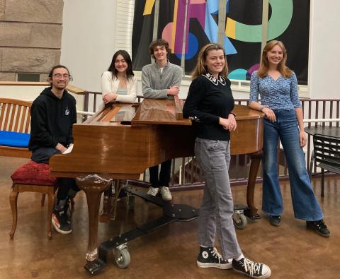 Students standing around a piano