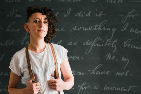 The artist standing in front of a chalkboard with writing on it