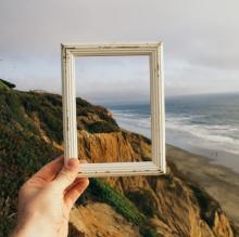 person holding a picture frame in front of an ocean landscape