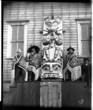 Image of three men sitting next to a totem pole