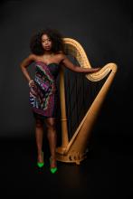 Artist standing with a harp in front of a black background