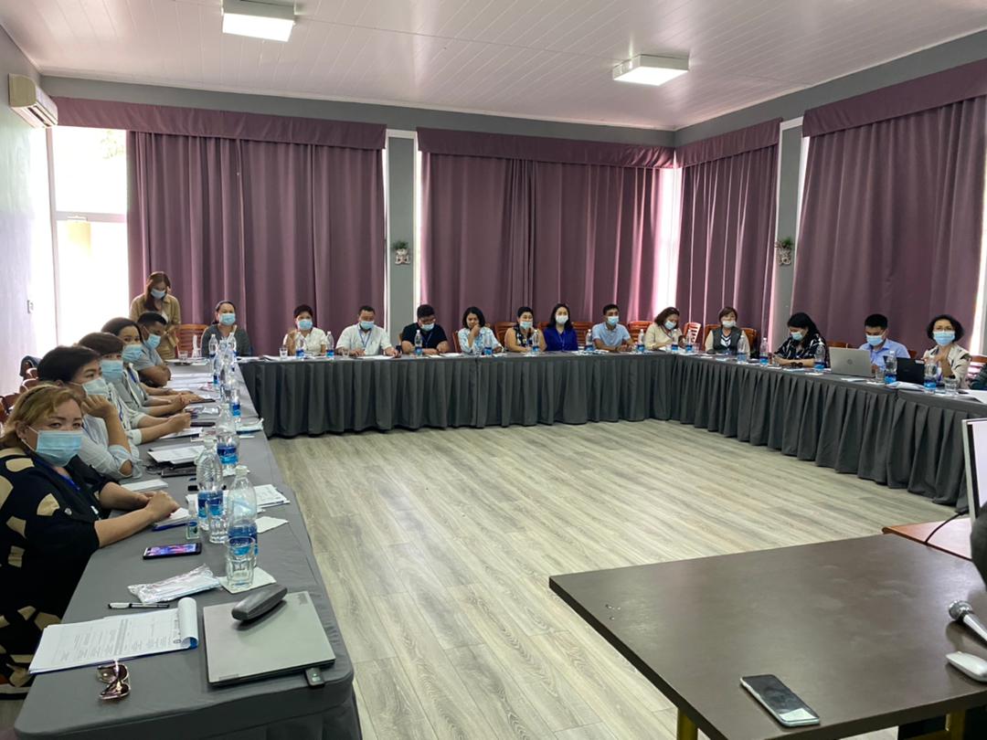 Room of masked people sitting around a large conference table