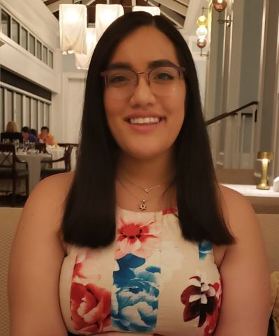 Megan Spitzer looking happy and smiling, wearing glasses, long black hair, in an indoor setting with skylights