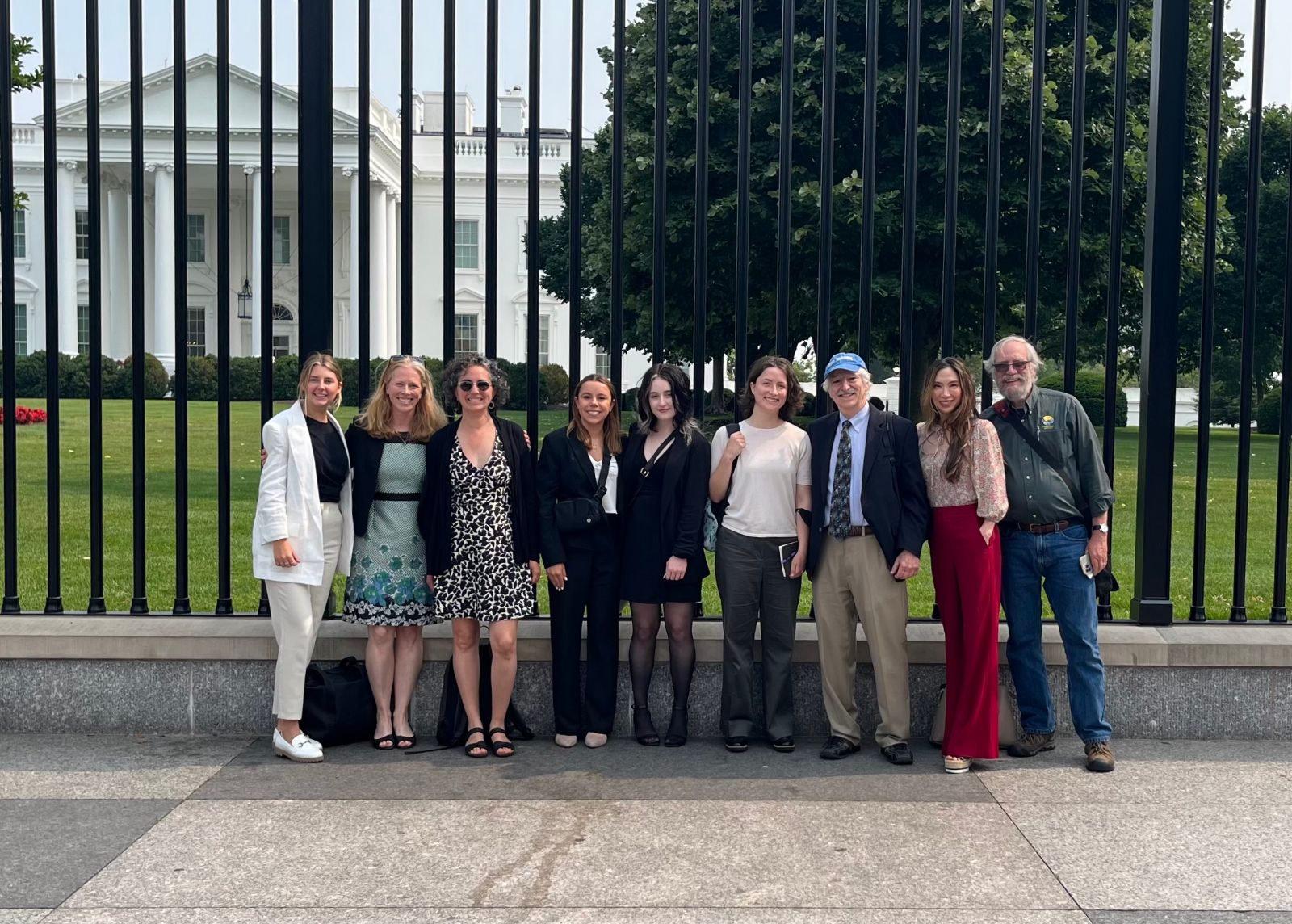 Group of people standing in front of white house, huge metal bars of the fence surrounding behind