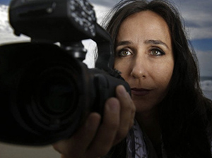 Filmmaker Gabriela Cowperthwaite in partial shadow behind her camera looking out thoughtfully