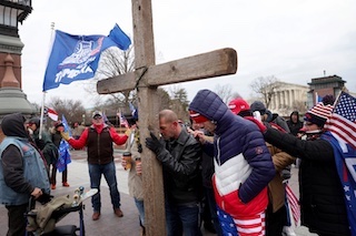 Men and women dressed in winter clothing holding american flags and brandishing a body size cross