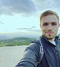 Kevin Heller, smiling wryly, taking a selfie on a big, beautiful beach