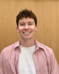 Nate looking cheerful smiling brightly against a wood panel background