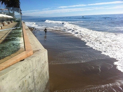 surfer walking on beach next to seawall