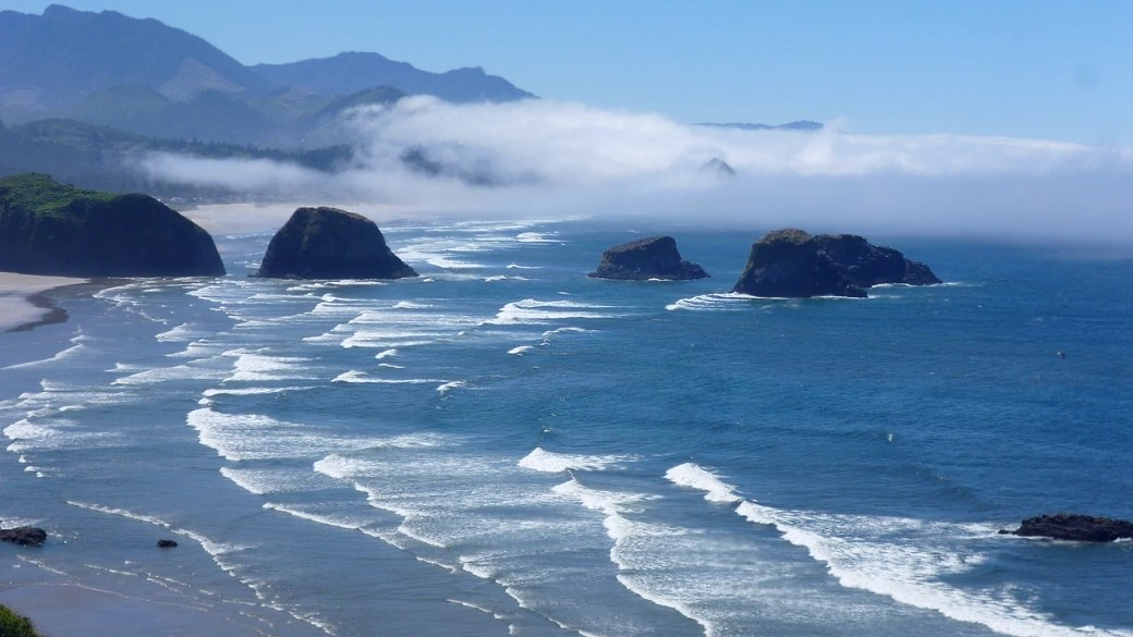 Sunny, waves, large rocks, and fog lifting in front of a mountain