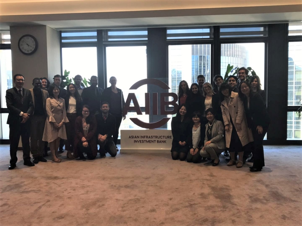 Group of students and professors standing around a sign for the Asian Infrastructure Investment Bank. The sign is red.
