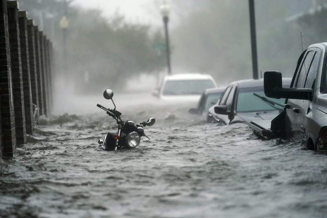 City street showing a motorcycle and cars mostly under water from storm surge and flooding