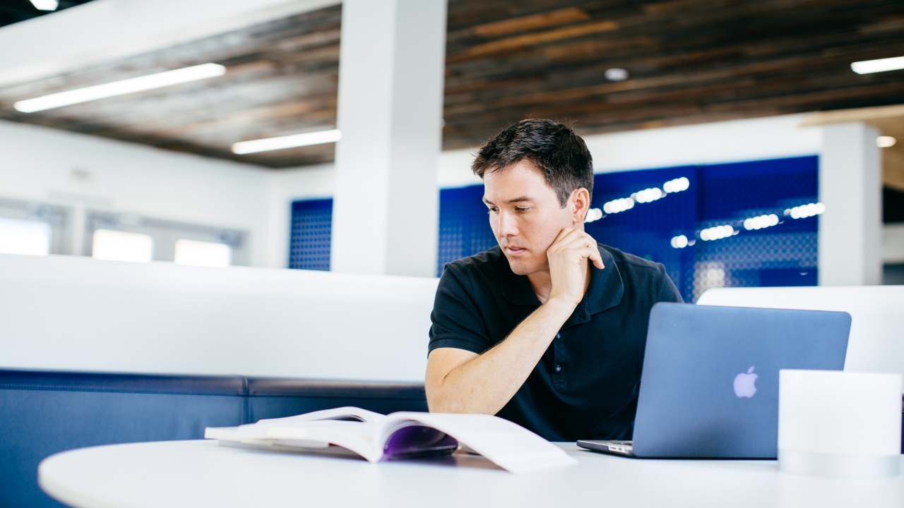 Student reading a book with laptop open