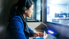 A young female student speaking into a mic in a broadcast studio.