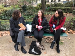 Three people are talking in a park in Paris while sitting on a bench eating food.