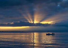 Fisherman at Sunrise on a broad sea, big sky, light rays from the sun