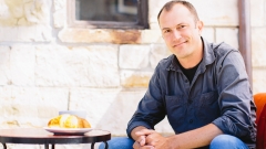 Scott Webb, sitting and smiling, while enjoying a croissant and coffee