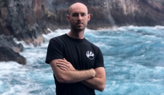 Profile image of Cameron Steagall standing, arms folded, by the ocean