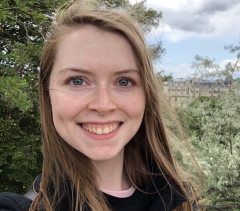 Headshot of Mariah Rust, smiling and standing outside with trees and a building in the background