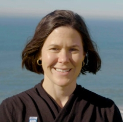 Commander Meaghan Brosnan, Marine Program Director, WildAid smiling and looking smart and capable with short brown hair windswept against the backdrop of the sea