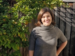 Profile image of Lacey Raak, standing outside by a plant-covered wooden fence