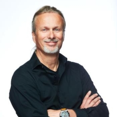 Dr. Gulio De Leo with arms crossed in a black shirt against a white background, looking confident, smiling