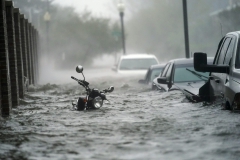 City street showing a motorcycle and cars mostly under water from storm surge and flooding