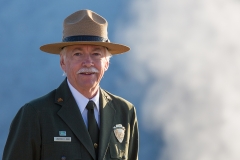 Jonathan Jarvis looking dapper in his National Parks Service uniform and broad brimmed hat, he is a white haired gentleman with a white mustache, posed for the photo against a cloud filled sky