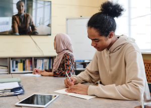 Students sitting at a classroom table writing on a paper