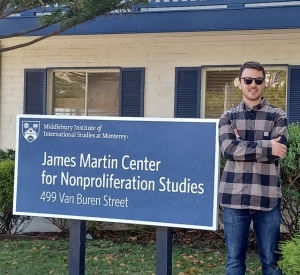 A MIIS student stands wearing sunglasses in front of the blue sign for MIIS' NPST studies building