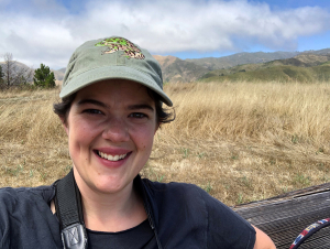 Ellie Oliver smiling and looking happy in a windy tundra, cap on, camera around her neck