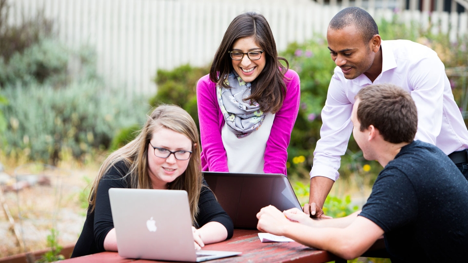 Students around a table outside look at their computers.