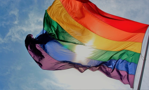 Rainbow flag flyer against a blue sky with sunlight behind