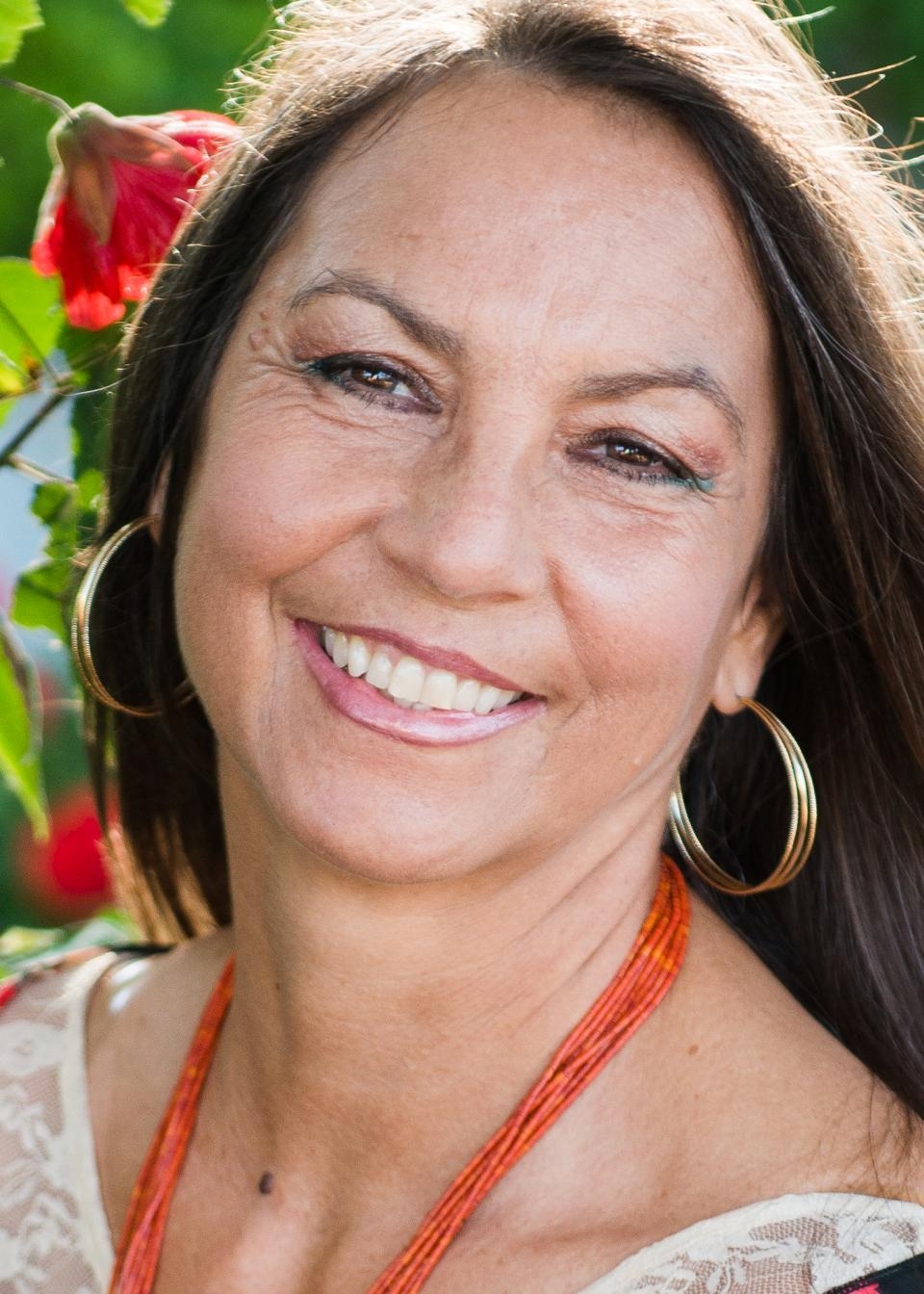 Headshot of Ms. Dina Gilio-Whitaker, smiling and with smiling eyes, head tilted, sun on her hair