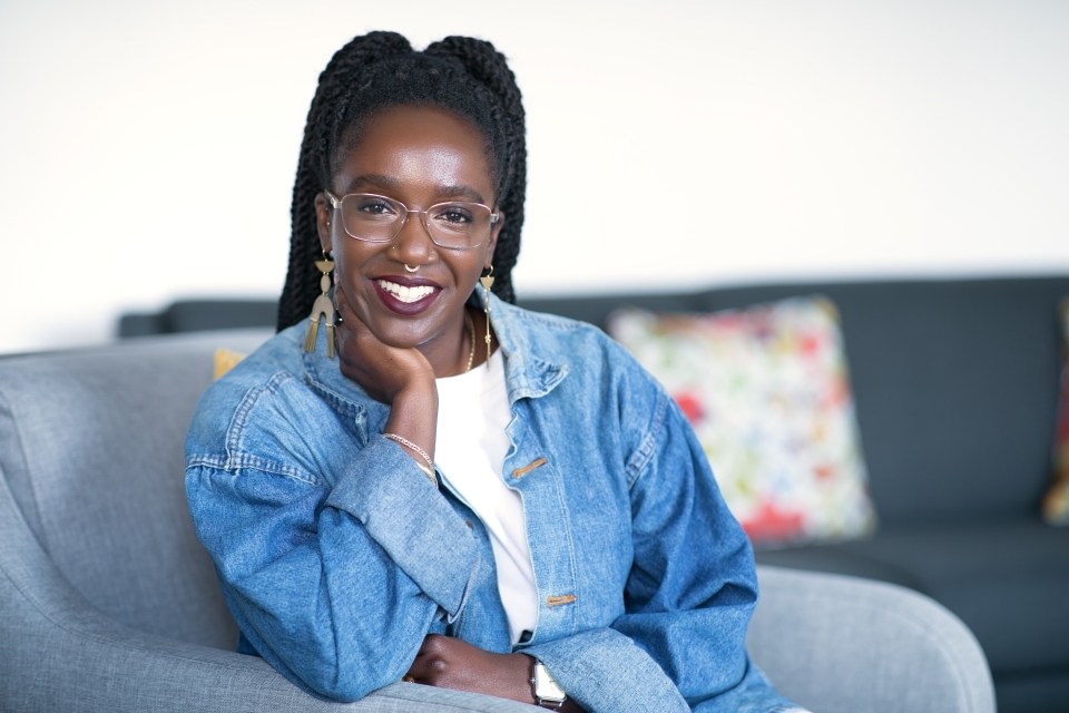 Ms. Nwamaka Agbo sitting on her couch, stylish and young, smiling and intelligent looking