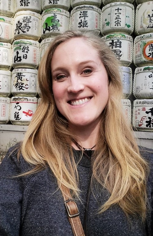 Aimee Kerr, smiling and looking kind, standing in front of a shelf of Japanese labeled cans