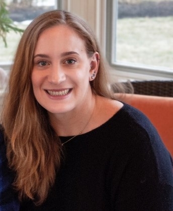 Emma Shipley smiling brightly, looking directly at the camera confidently, long hair over right shoulder, black shirt