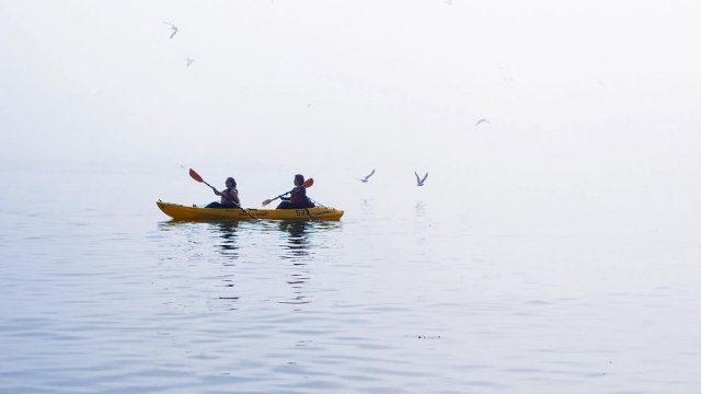 Two people on a kayak in the middle of a lake at sunrise.