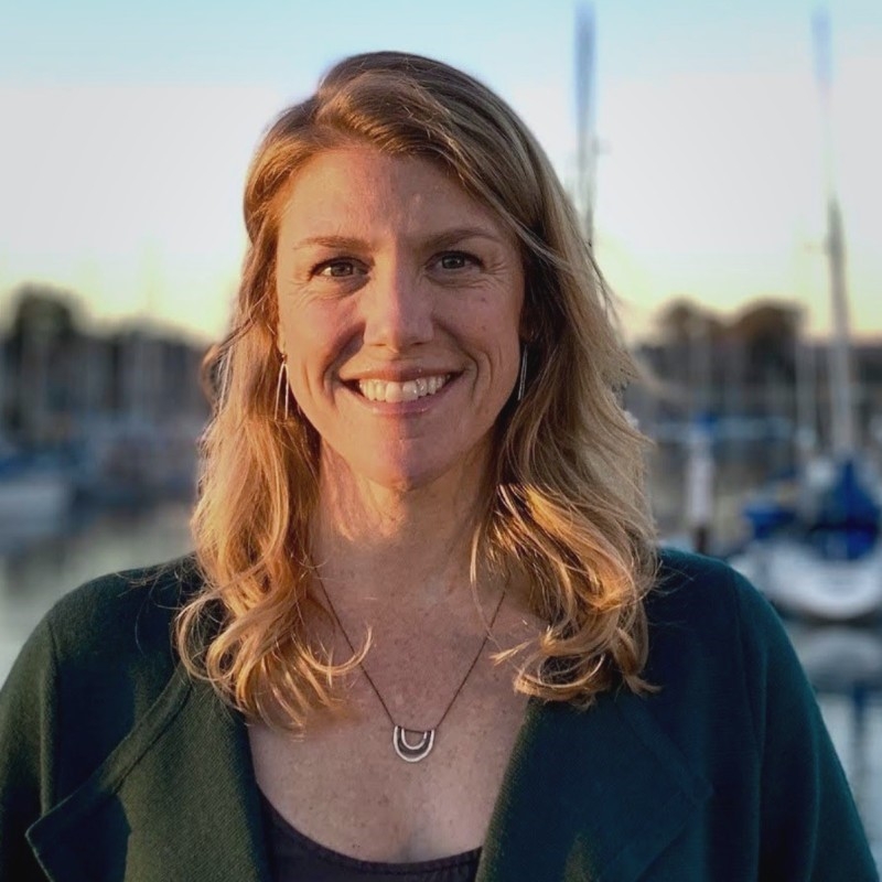 Sara Pfeifer smiling brightly with golden sun on her face, with boats at a harbor in the background