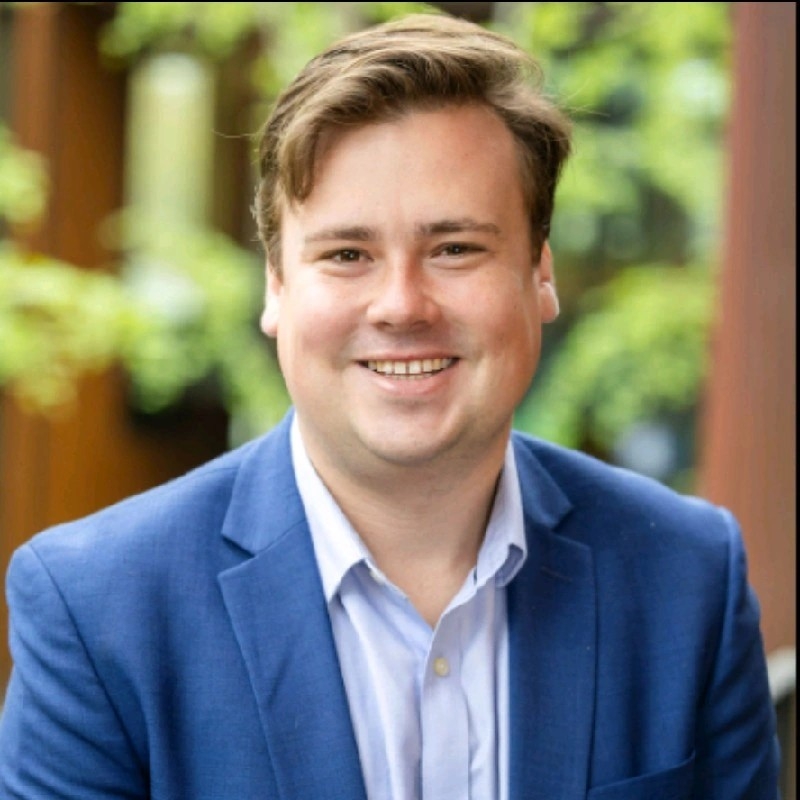 Sam Naujokas smiling brightly looking sharp in a blue suit jacket