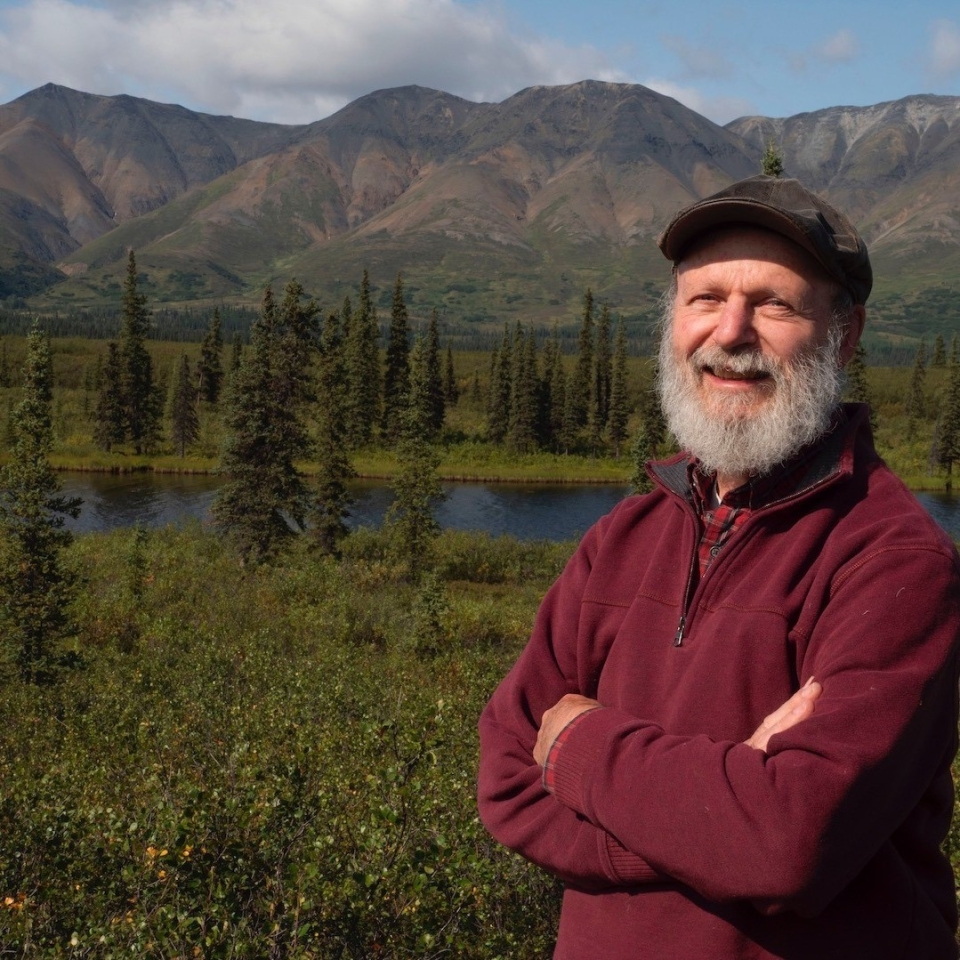 Dr. Terry Chapin looking cheerful, smiling in the setting sun, arms crossed, standing in a beautiful alpine lake setting