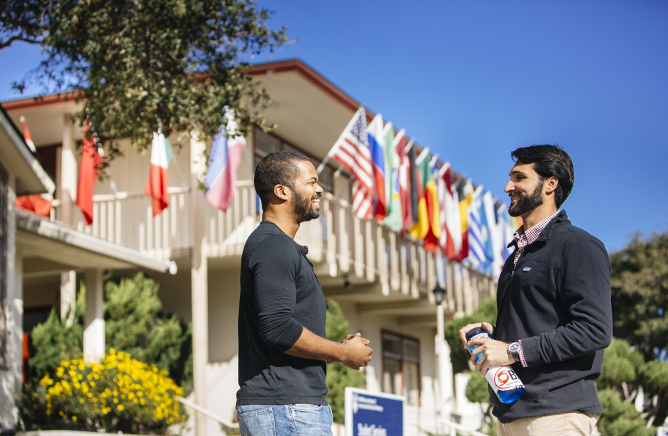 Two students standing in front of the Morse building, which is lined by flags of different countries